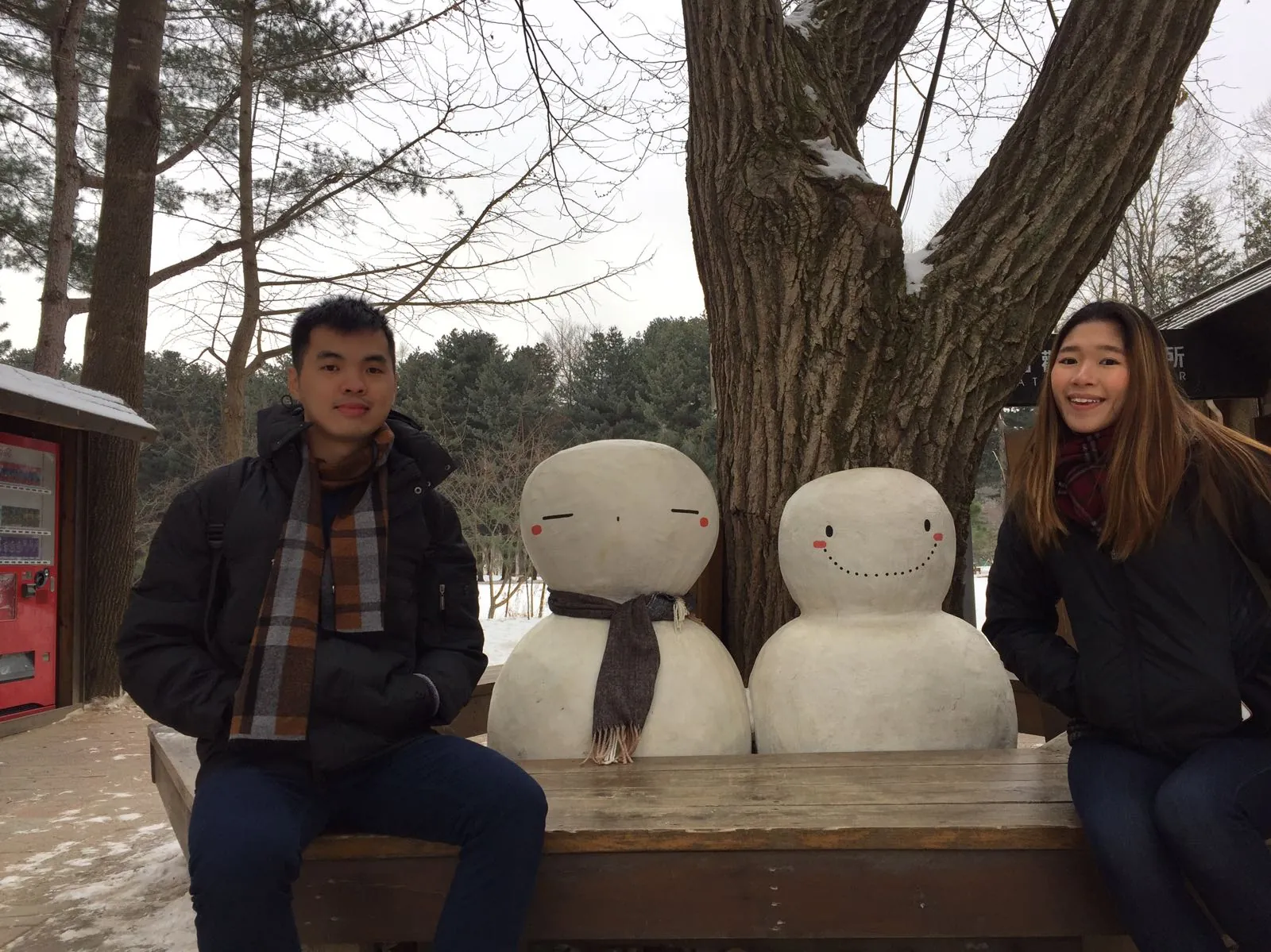 Nicholas and his wife sitting beside snowman sculptures on Nami Island