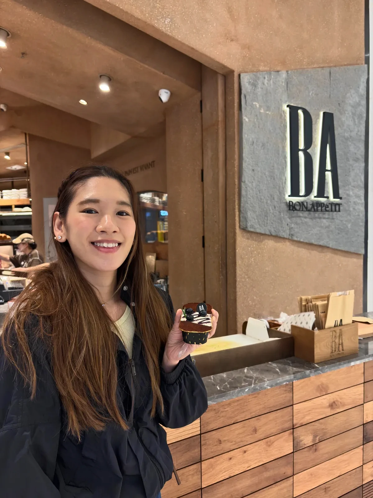Woman holding a cupcake at a Bon Appetit bakery counter