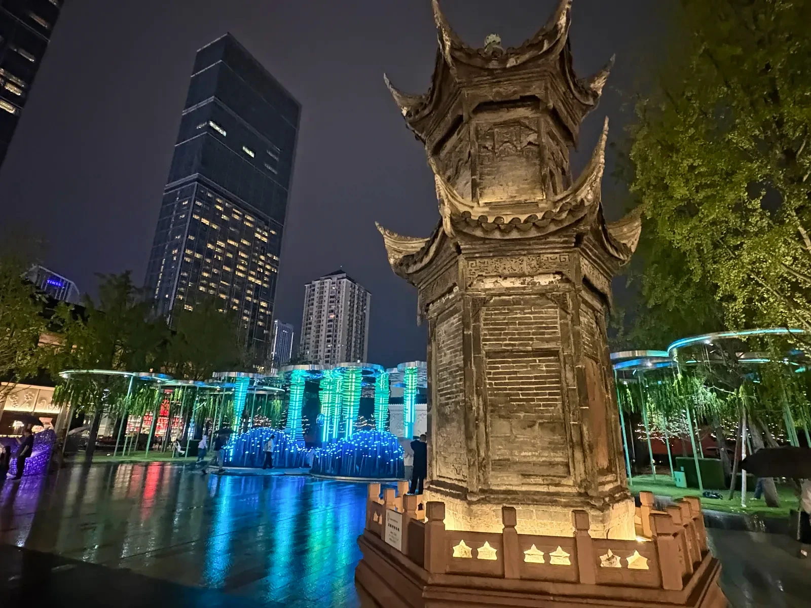 Old stone ziku tower, once used to burn paper bearing writing, lit up beside light installations and modern towers at Taikoo Li
