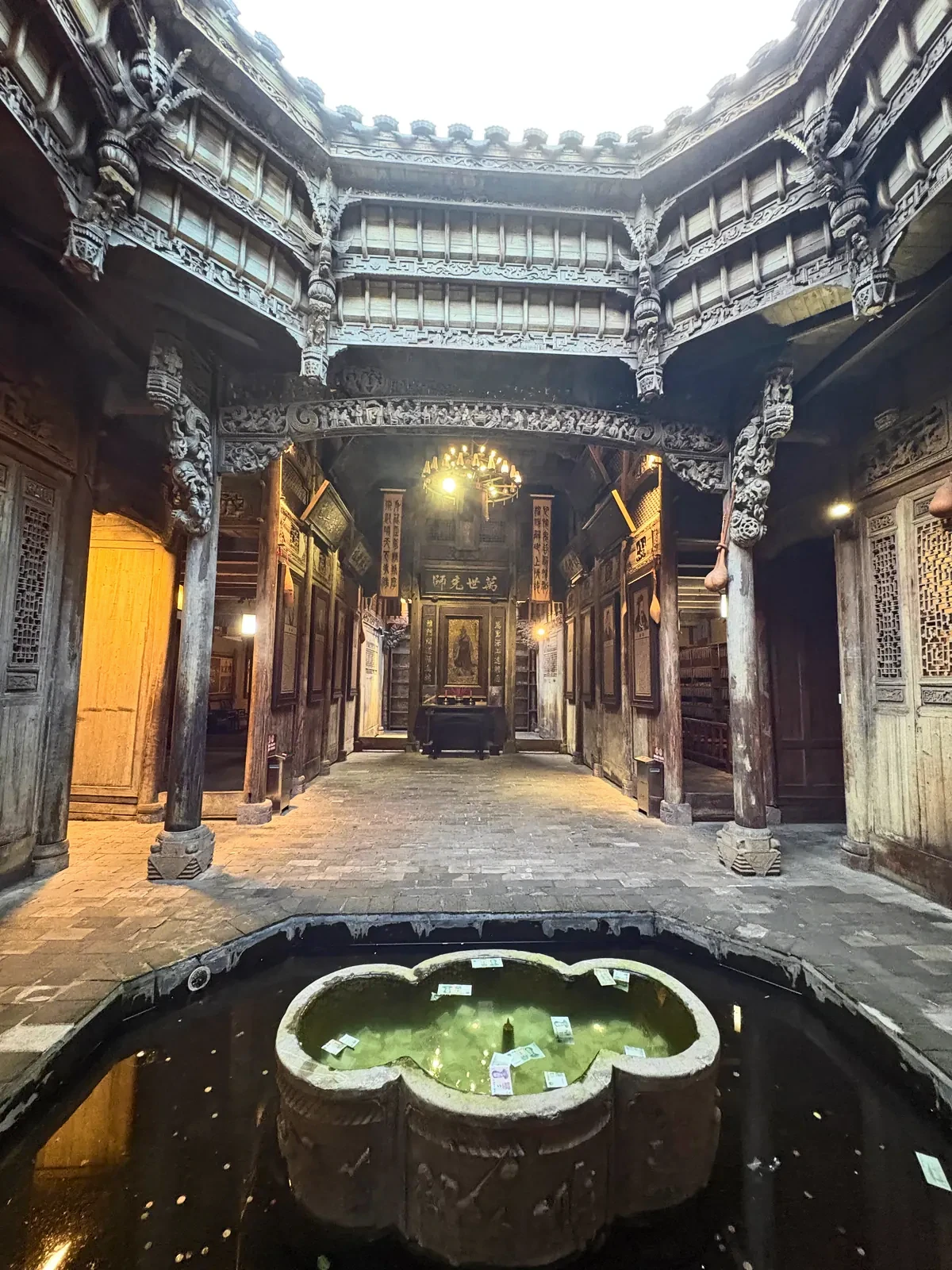 Carved wooden courtyard with a stone basin of coins and notes at its centre