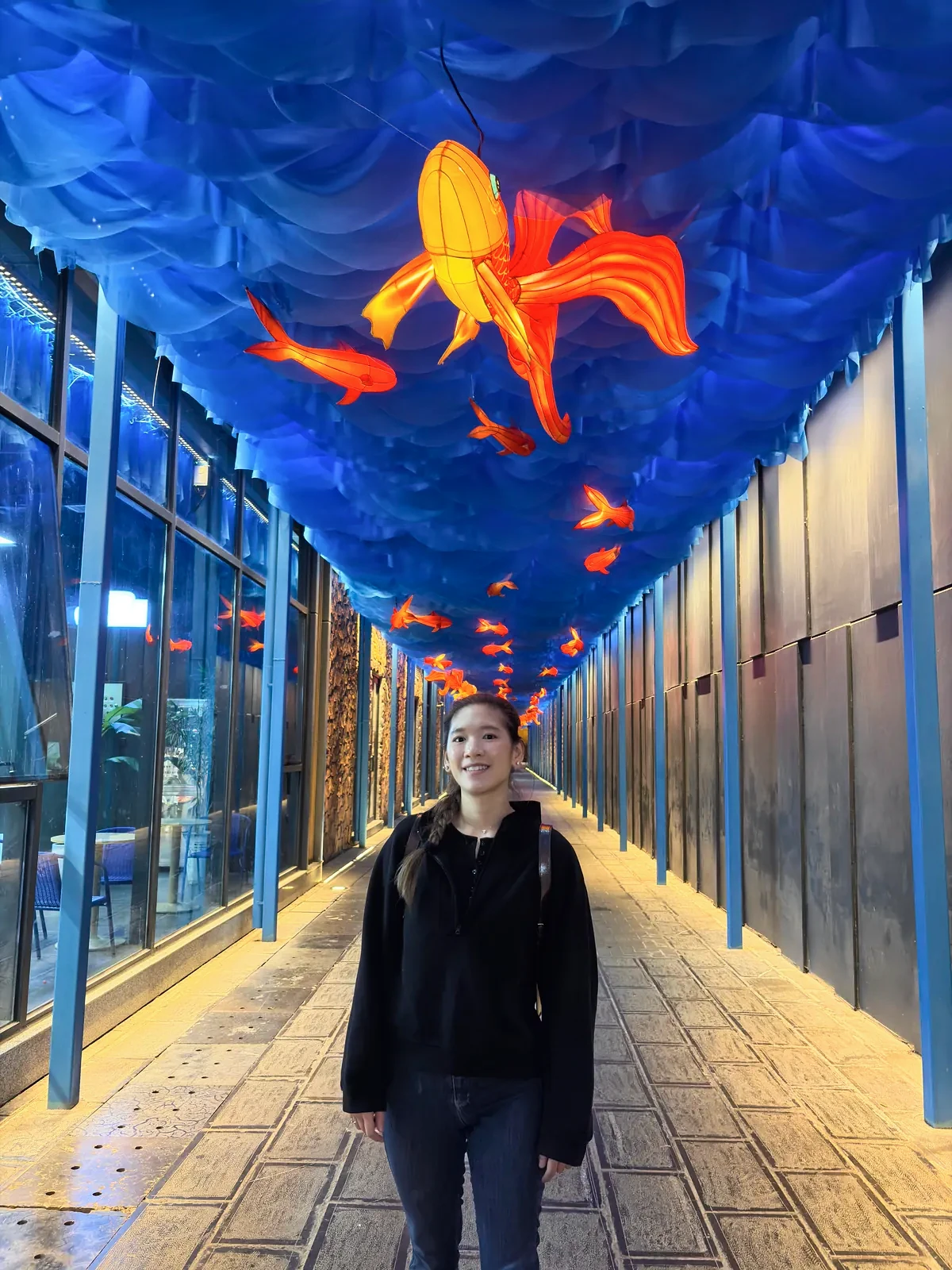 Woman beneath glowing orange fish lanterns in a blue-lit passage